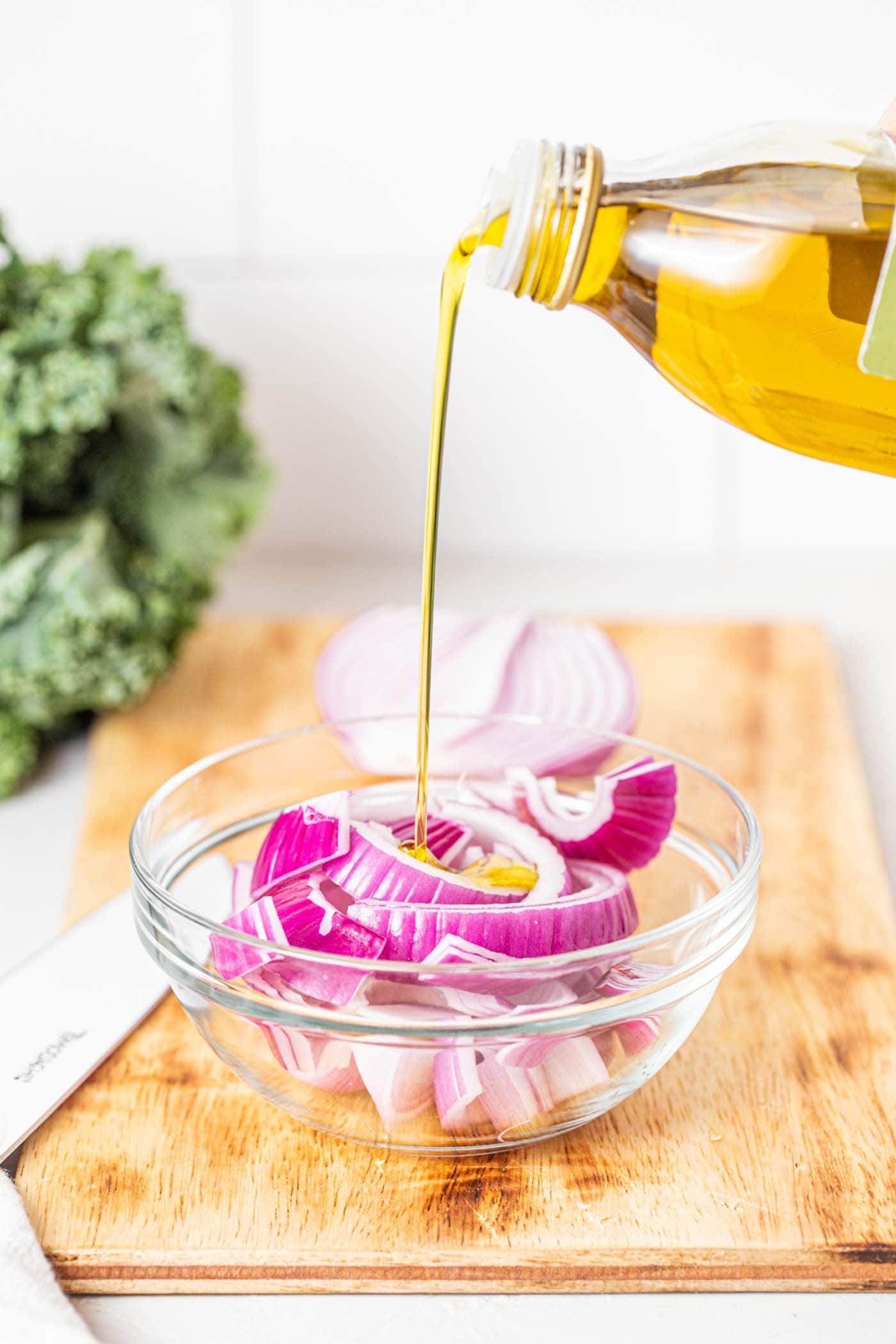 Crispy Buffalo Cauliflower Kale Salad 6 A close-up of sliced red onions in a glass bowl, being coated with a generous pour of olive oil, before seasoning and roasting.