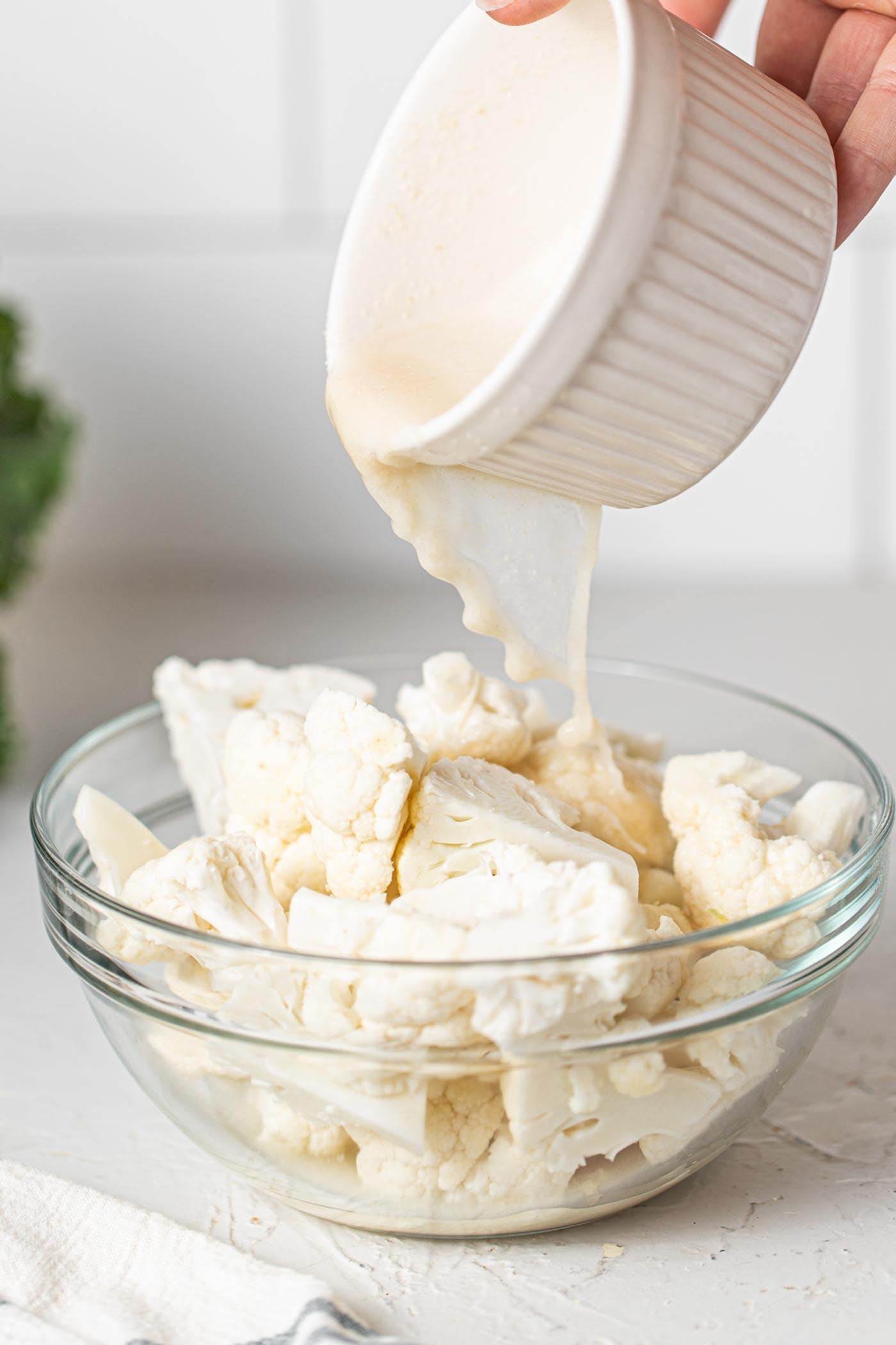 Crispy Buffalo Cauliflower Kale Salad 4 Pouring a milky batter over chopped cauliflower in a clear glass bowl, ensuring each floret is coated for baking.