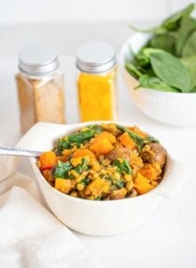 A bowl of butternut squash and lentil stew with mushrooms and spinach.