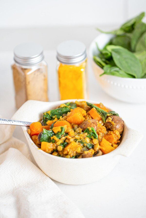 A bowl of butternut squash and lentil stew with mushrooms and spinach.