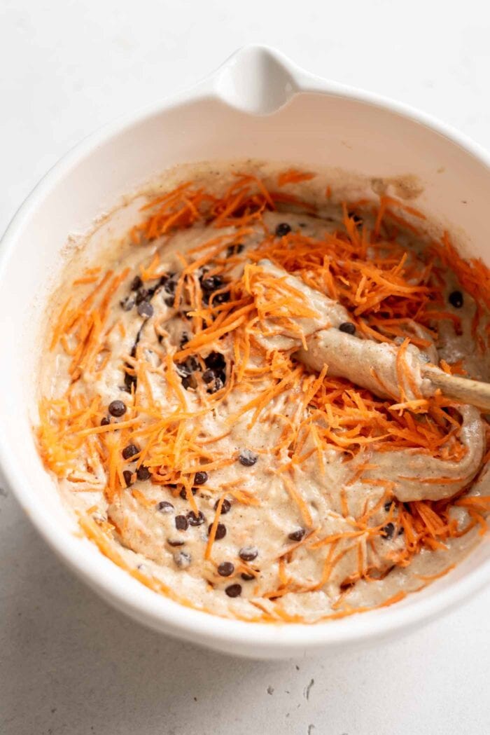 Raw muffin batter with chocolate chips and grated carrot in a mixing bowl.