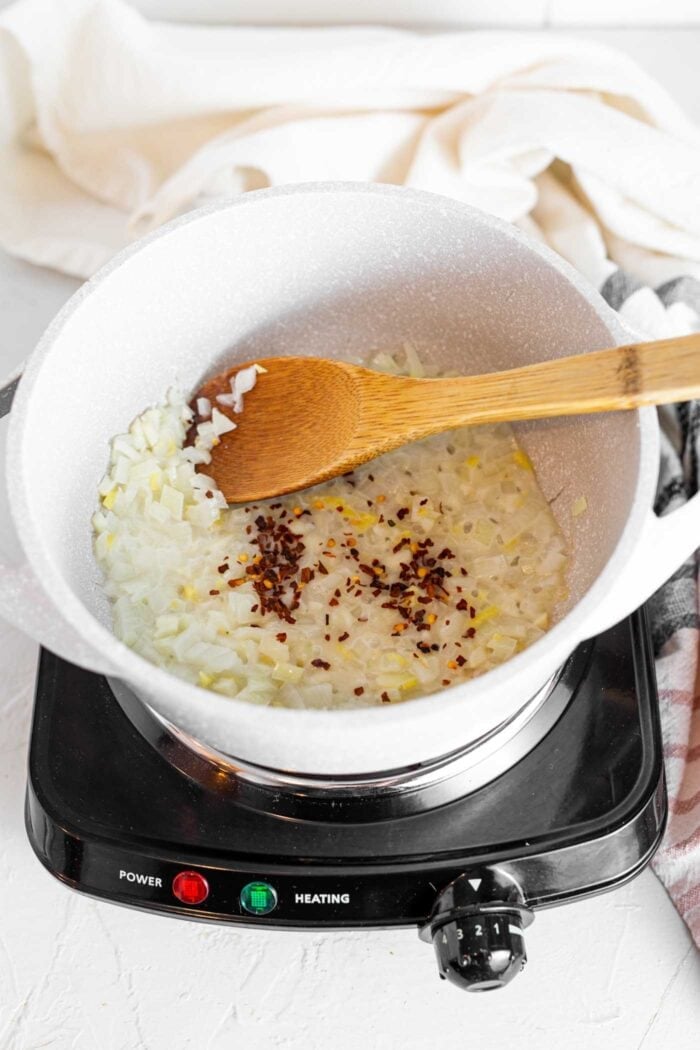 Onions and garlic cooking in a large soup pot with a wooden spoon.