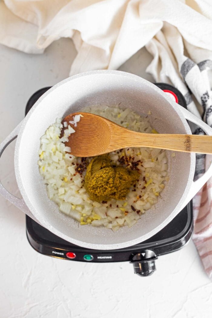 Stirring green curry paste into a pot with onions and garlic.