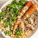 Roasted carrots, kale, quinoa, chickpeas and pumpkin seeds in a bowl topped with tahini sauce.