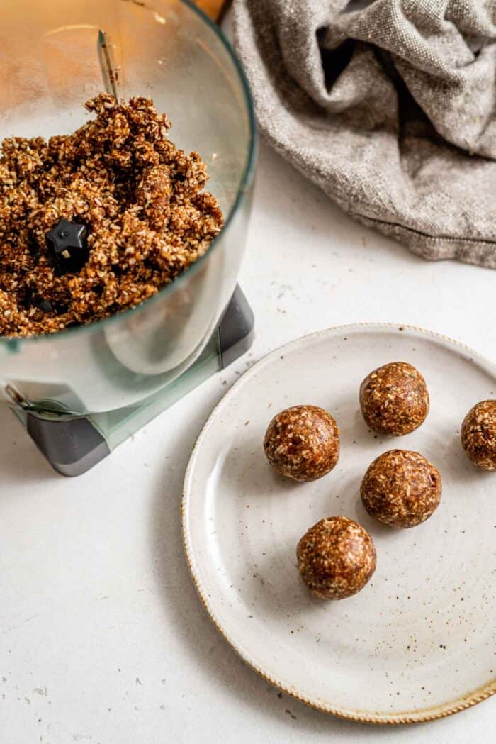 Rolled energy balls on a plate beside a food processor full of dough.