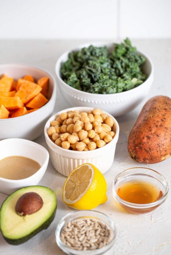 Kale, chickpeas, sweet potato, lemon and avocado on a counter.