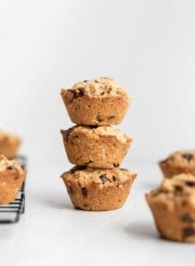 A stack of 3 small muffins on a counter beside a cooling rack.