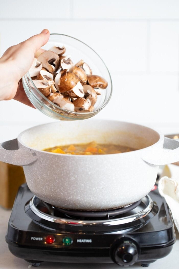 Adding chopped mushrooms to a large bowl of stew.