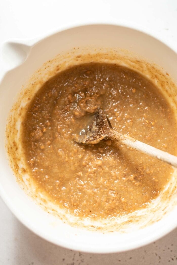 Almond butter mixing with applesauce and maple syrup in a mixing bowl with a spoon.