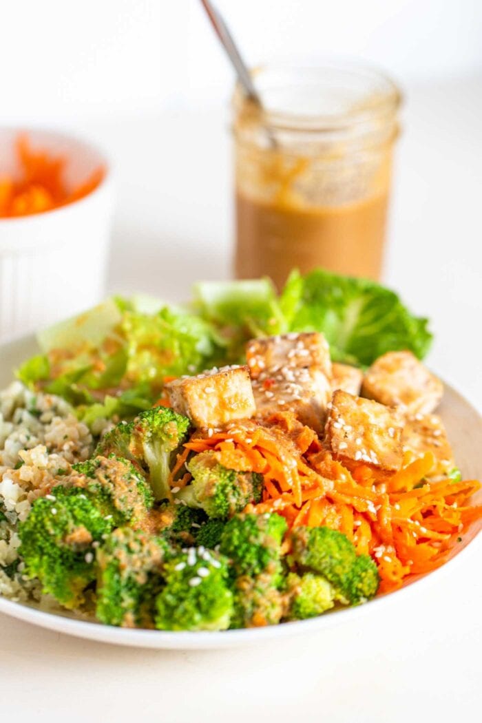 A bowl with carrot, tofu, broccoli, cauliflower rice, tofu and peanut sauce.