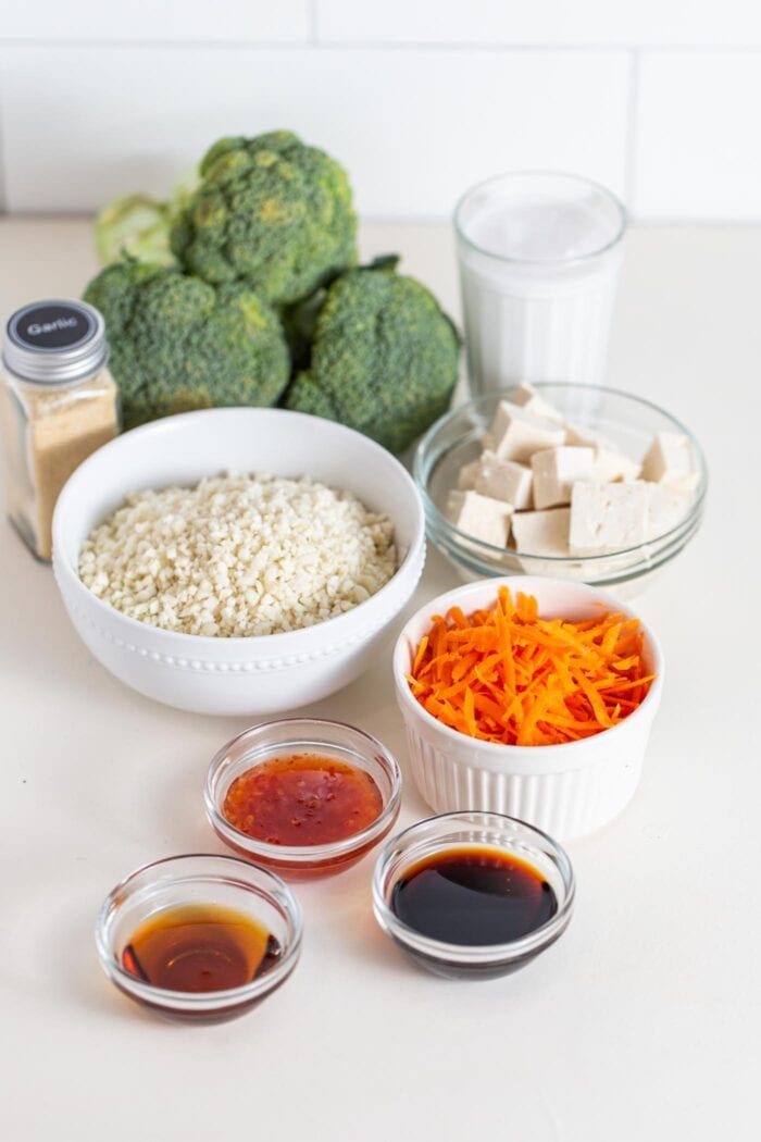 Broccoli, cauliflower rice, carrot, tofu and sauce in containers on a counter.