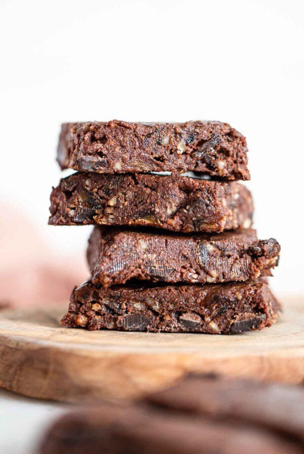 A close up of a stack of 4 raw brownies on a cutting board.