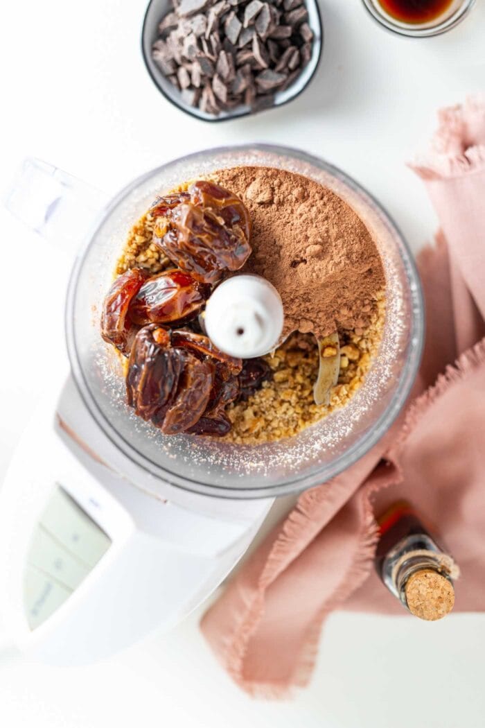 Cocoa powder, dates and walnuts in a food processor container.
