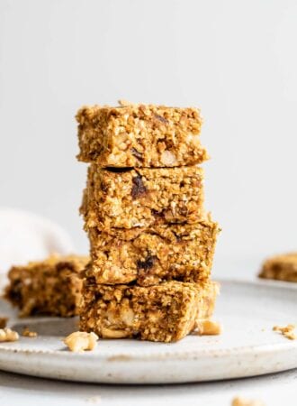 A stack of 4 pumpkin oat bars with dates and walnuts in them on a plate.