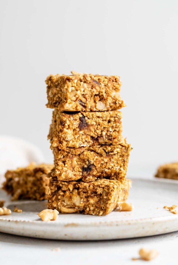 A stack of 4 pumpkin oat bars with dates and walnuts in them on a plate.