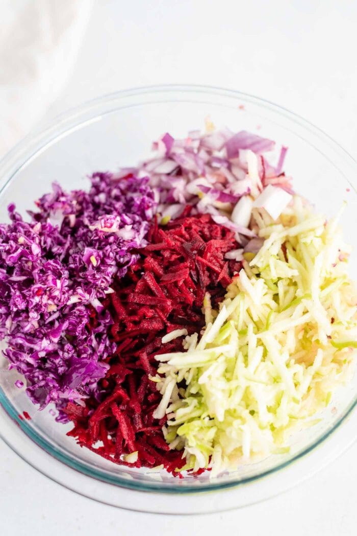 Shredded cabbage, beet, apple and red onion in a mixing bowl.