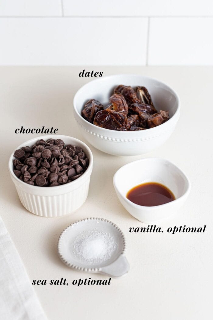 Chocolate, dates, vanilla and sea salt in small bowls on a counter.