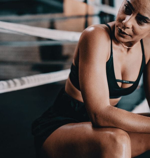 Fit women in a sports bra sitting and looking off to the side.