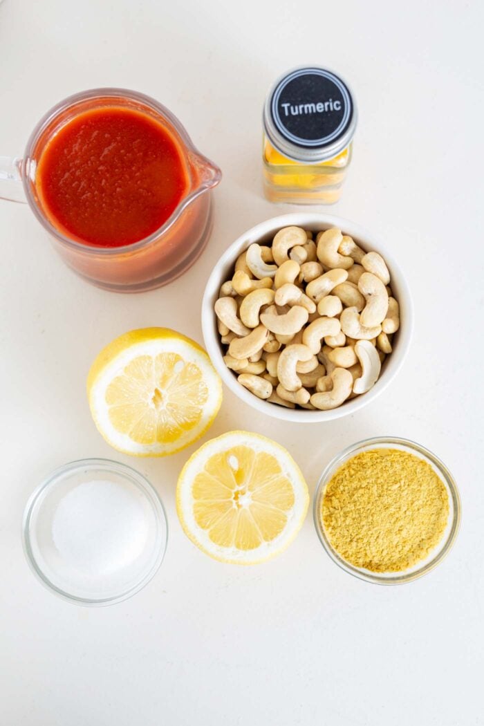 Cashews, nutritional yeast, lemon and tomato sauce in containers on a counter.