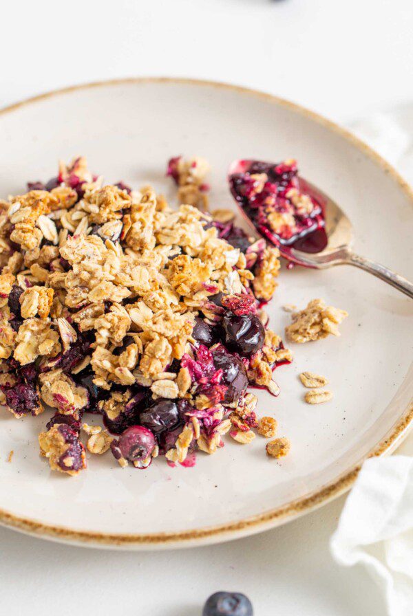 A serving of blueberry crisp on a plate with a spoon.