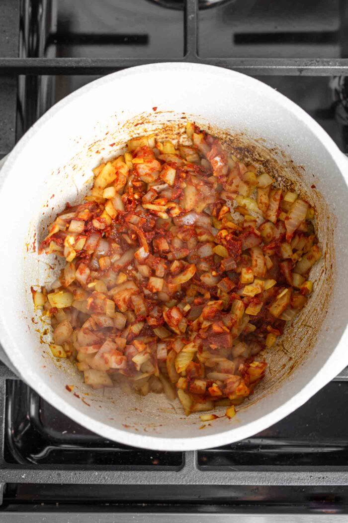 Onion, garlic, ginger and tomato paste cooking in a large soup pot on a gas range.
