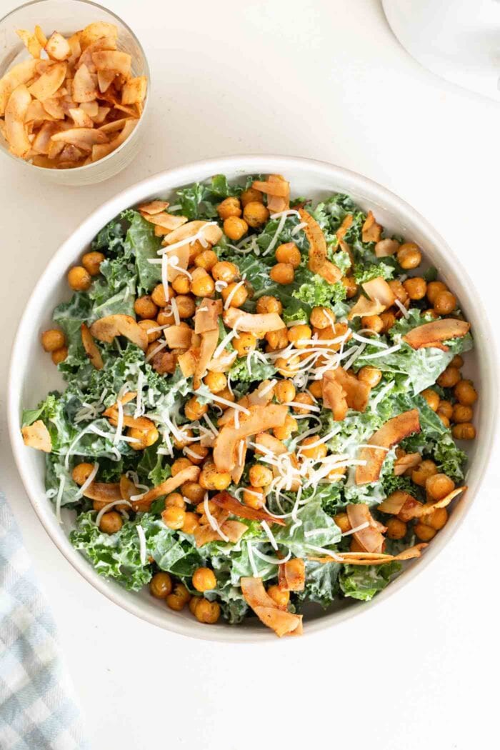 A large kale salad with dressing, chickpeas, parmesan and coconut bacon on top.