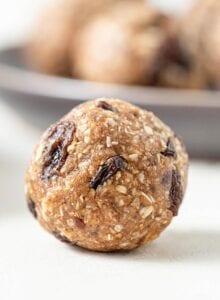 A close up of a cookie dough ball with raisins in it on a counter top.