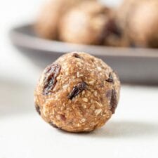 A close up of a cookie dough ball with raisins in it on a counter top.