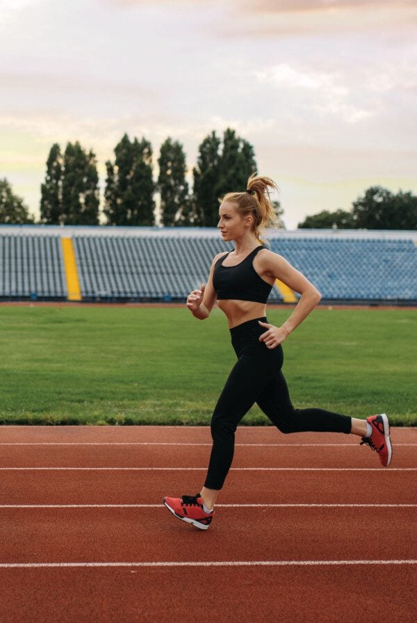 A fit woman in a sports bra and tights running on a track.