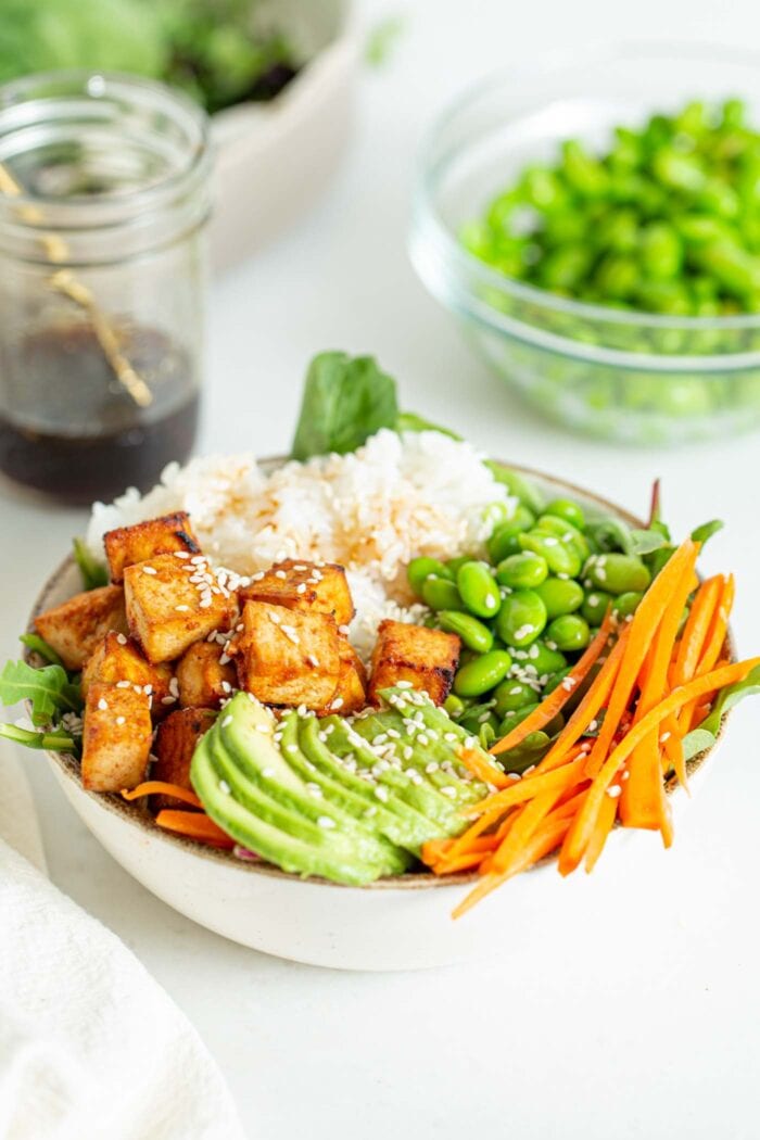A bowl with tofu, avocado, carrot, edamame and rice.