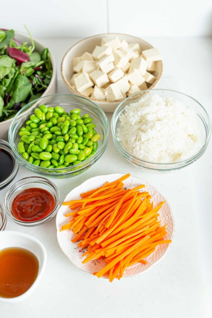 Sliced carrot, edamame, rice and tofu in bowls.