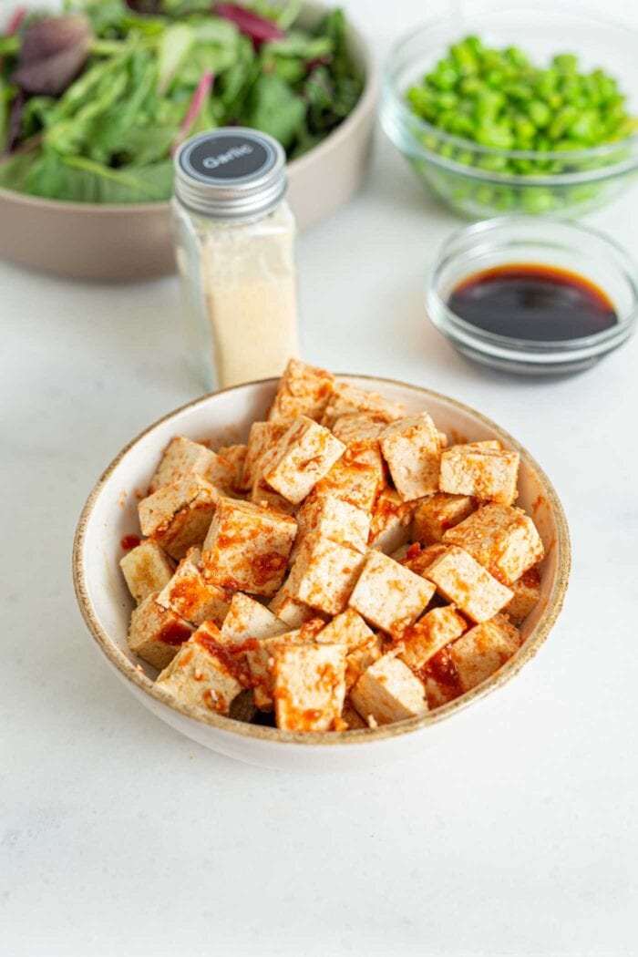 Cubed tofu in a bowl mixed with sriracha and garlic powder.