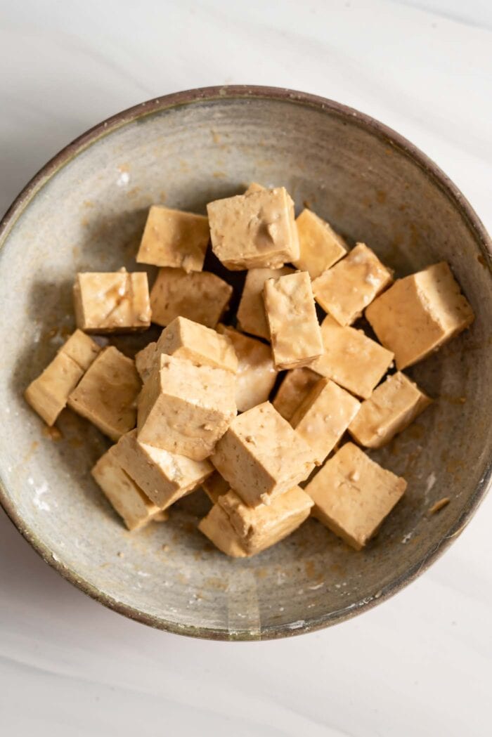 Tofu coated in cornstarch and soy sauce in a bowl.