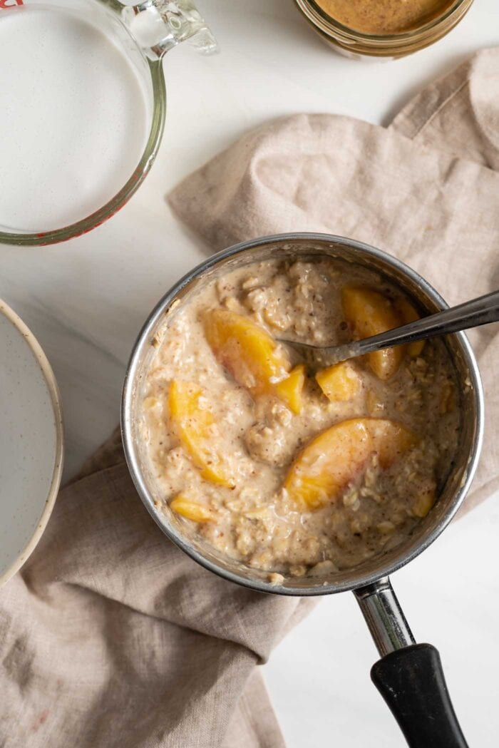 Cooked oatmeal with peaches in a saucepan.