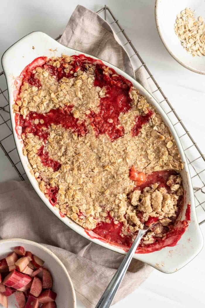 Rhubarb crisp in an oval baking dish with a spoon.