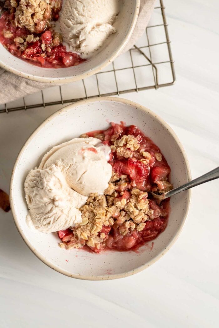 Bowl of rhubarb crisp topped with ice cream beside a cooling rack.