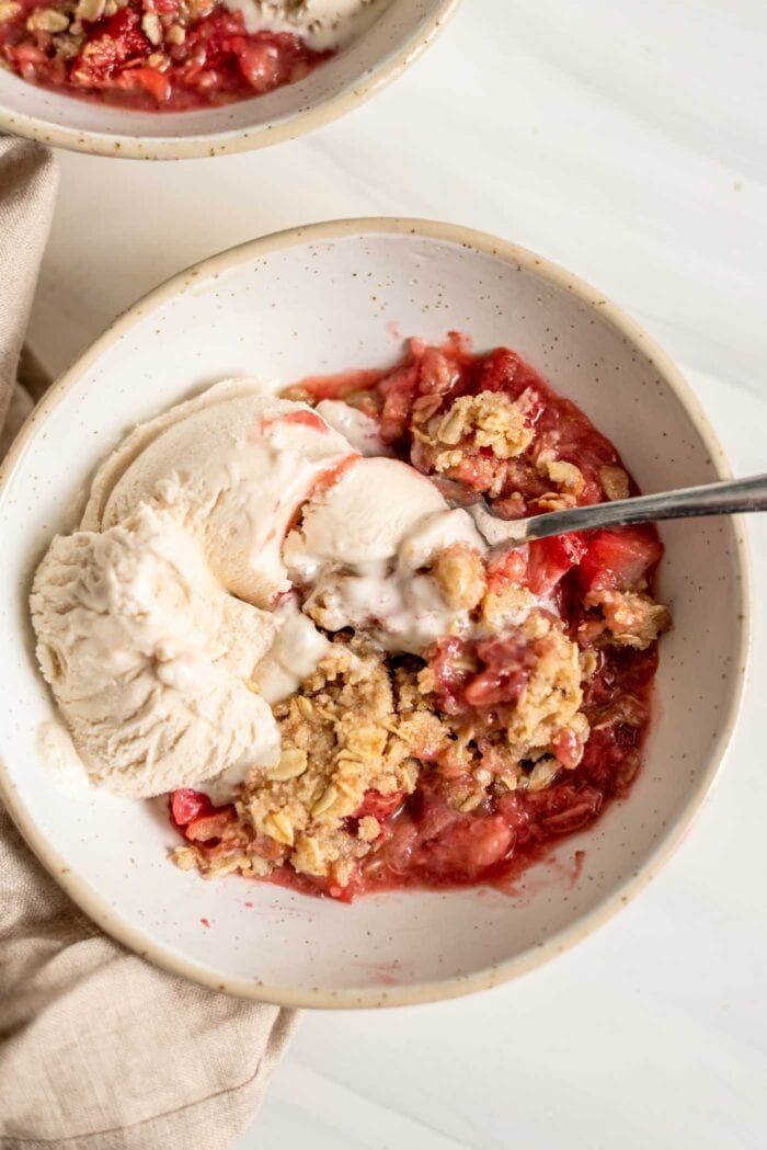 A bowl of strawberry rhubarb crisp with vanilla ice cream and a spoon in it.