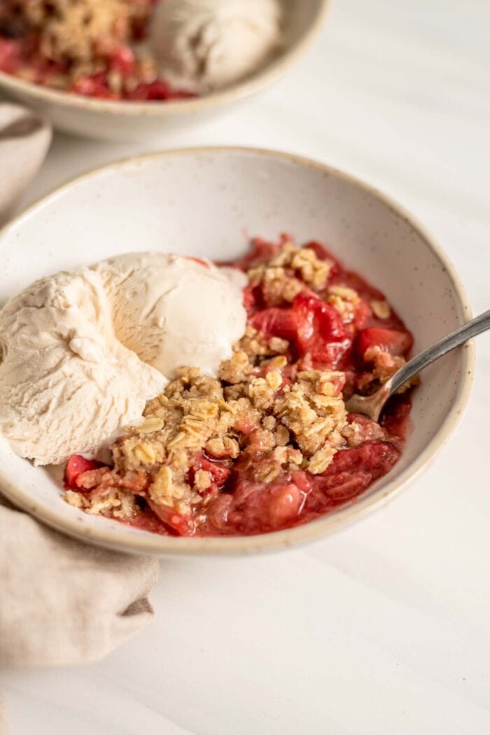 A bowl of strawberry rhubarb crisp with vanilla ice cream.