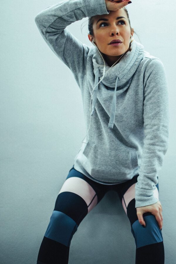 A fit woman in workout clothes leaning up against a wall.