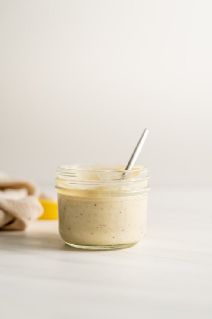 A glass jar of caesar salad dressing with a spoon in it.