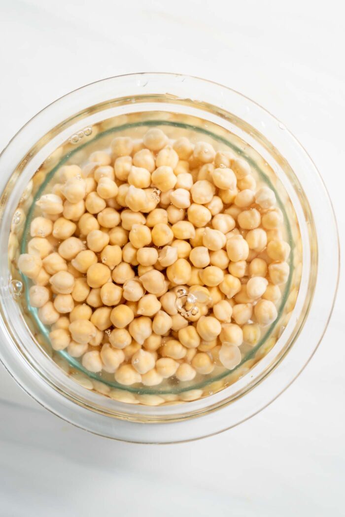 Chickpeas soaking in a glass bowl of water.