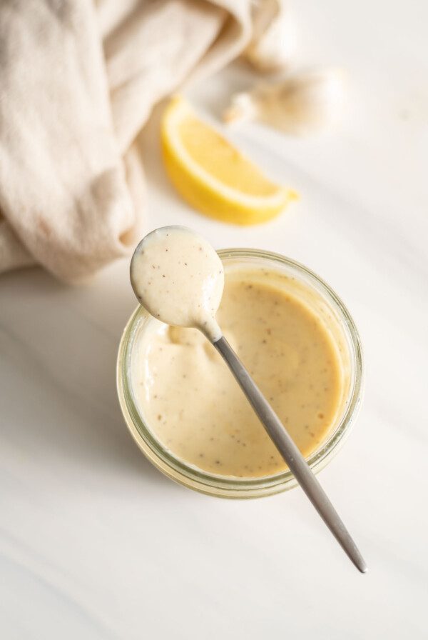 A spoonful of creamy caesar dressing resting on a jar of dressing.