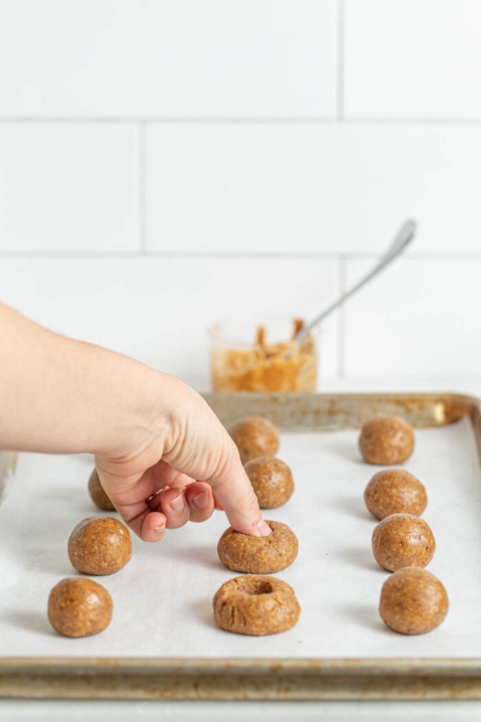 Pressing holes into cookie dough balls on a baking sheet.