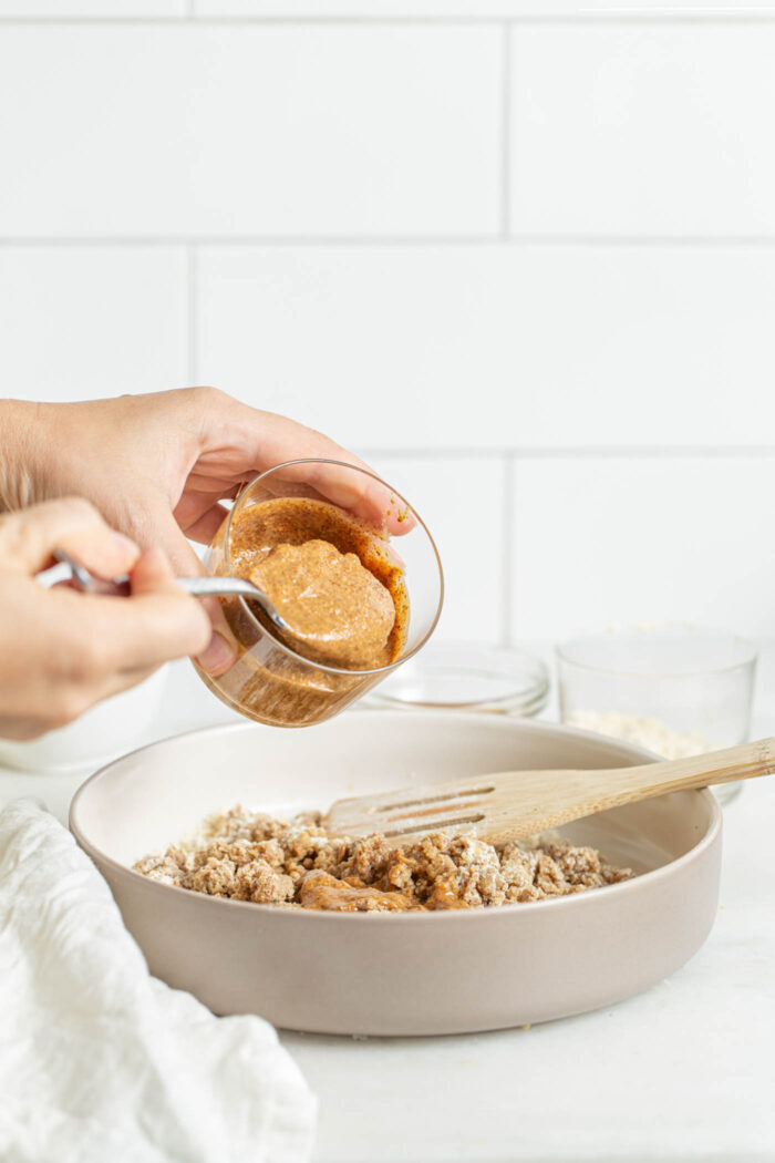 Scooping almond butter into a mixing bowl of cookie dough.