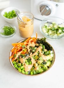 Carrot, edamame, rice, cucumber and nori topped with sauce in a bowl.
