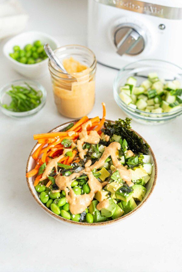 Carrot, edamame, rice, cucumber and nori topped with sauce in a bowl.