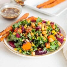 Bowl of kale salad with beet, corn, carrots and pumpkin seeds.