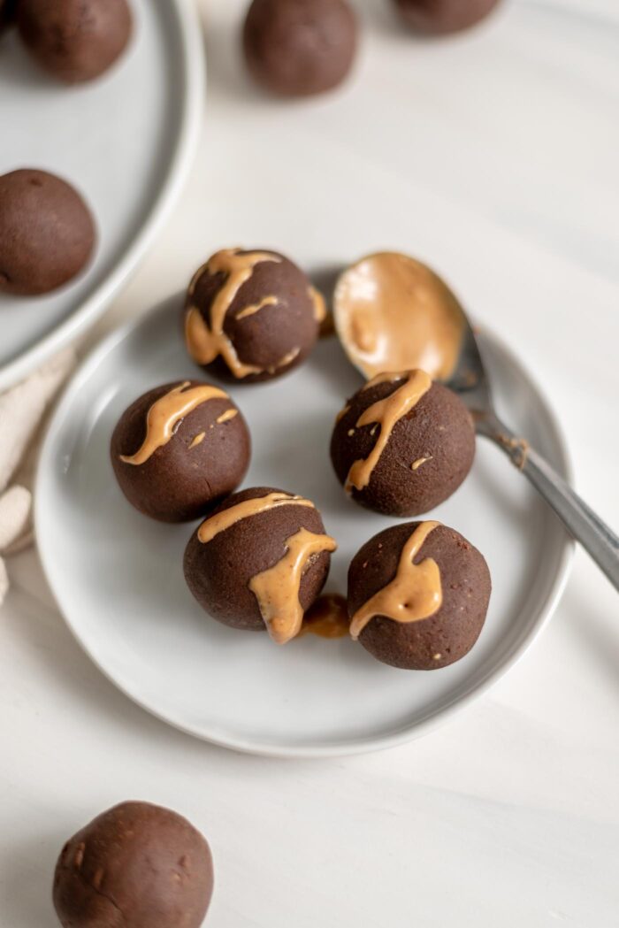 5 chocolate energy balls drizzled with peanut butter on a small plate.