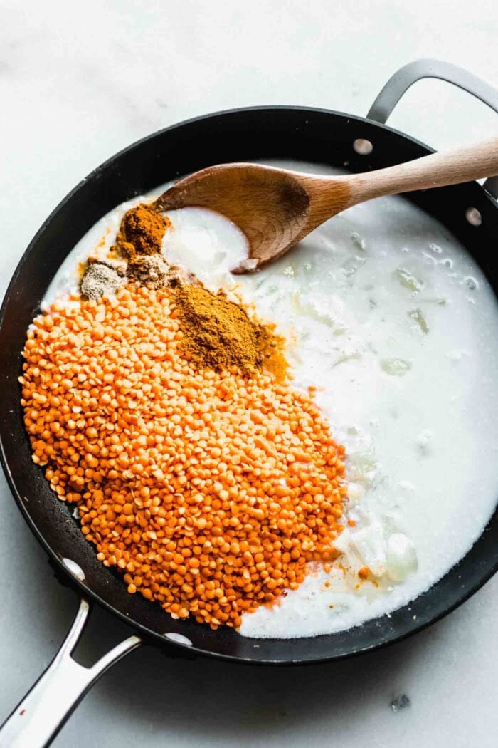 Lentils and coconut milk in a skillet with a wooden spoonl