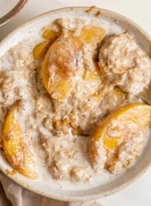 A bowl of peaches and cream oatmeal with a spoon in it.